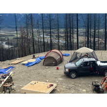 Load image into Gallery viewer, Two tents surround by an electric bear fence powered from a truck at an off grid construction site overlooking a valley.
